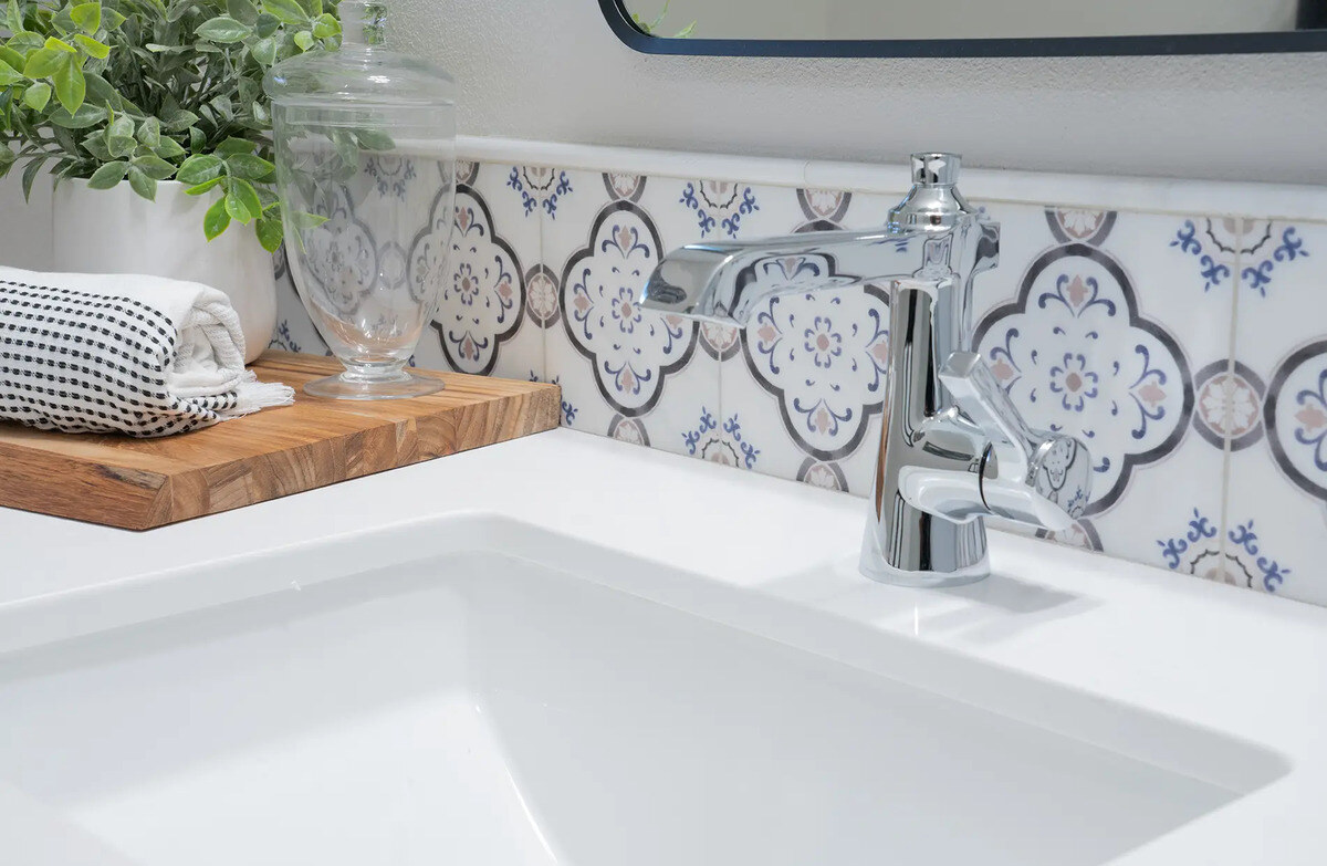 Up-close view of sink with stainless steel faucet and accent tile in bathroom by Imagine Remodeling